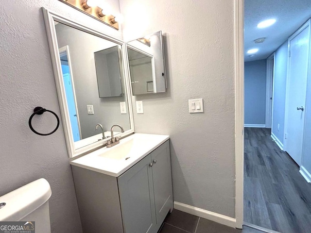 bathroom with toilet, a textured wall, vanity, and baseboards