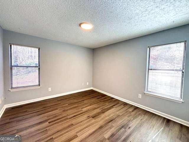 empty room featuring a healthy amount of sunlight, a textured ceiling, baseboards, and wood finished floors