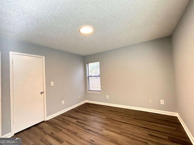 spare room featuring a textured ceiling, dark wood finished floors, and baseboards