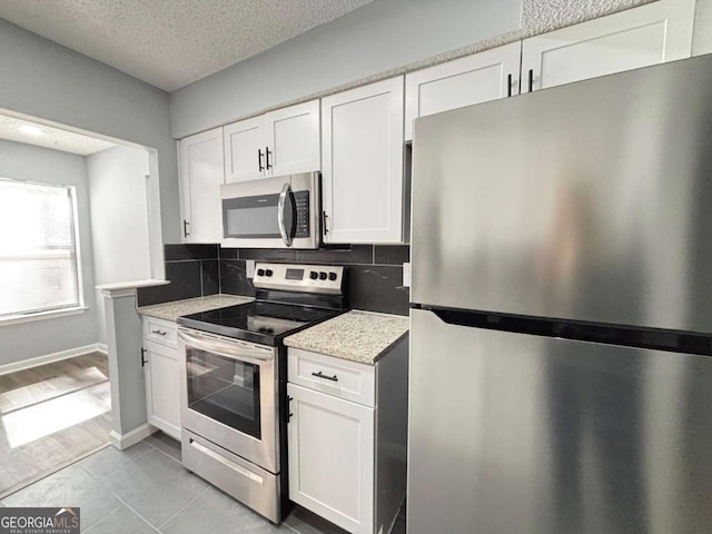 kitchen with white cabinets, decorative backsplash, light stone countertops, stainless steel appliances, and a textured ceiling