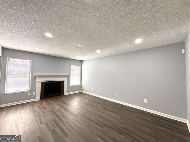 unfurnished living room featuring baseboards, dark wood-type flooring, a textured ceiling, a fireplace, and recessed lighting