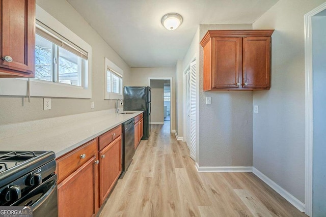 kitchen with baseboards, light wood-style flooring, brown cabinets, black appliances, and a sink