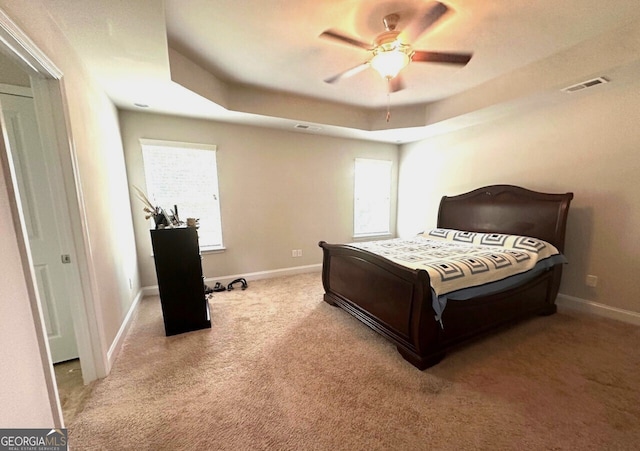 carpeted bedroom with a tray ceiling, baseboards, and visible vents