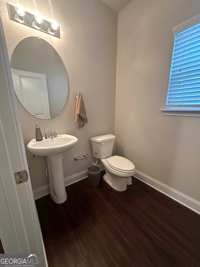 half bathroom featuring a sink, baseboards, toilet, and wood finished floors