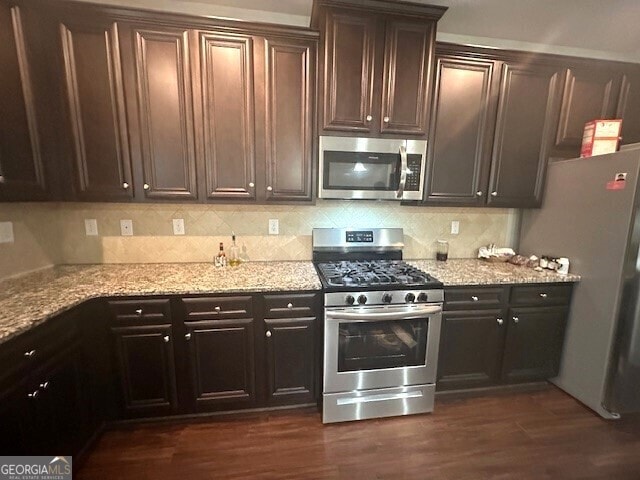 kitchen featuring dark brown cabinets, light stone countertops, decorative backsplash, appliances with stainless steel finishes, and dark wood-style floors