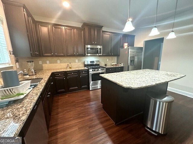 kitchen with dark wood-type flooring, a center island, stainless steel appliances, decorative backsplash, and light stone countertops