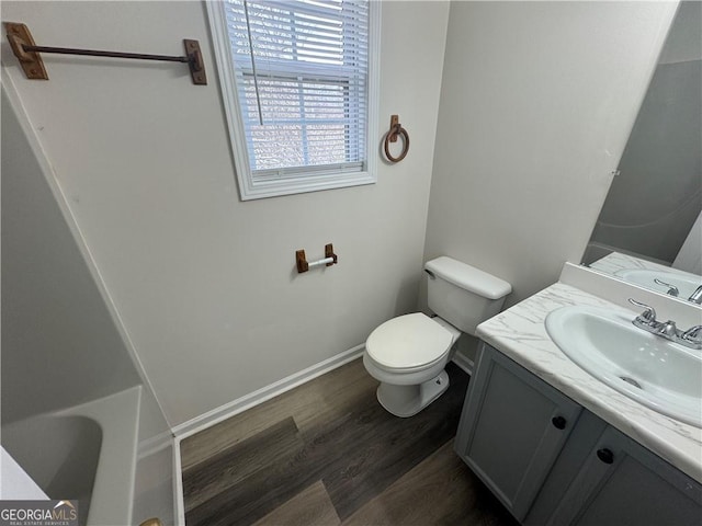 full bath featuring toilet, wood finished floors, vanity, baseboards, and a tub