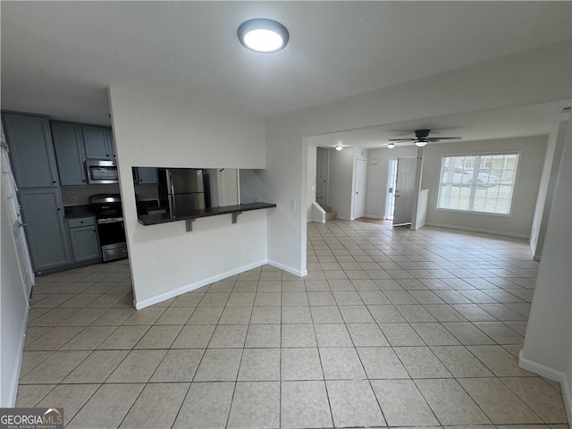 kitchen with light tile patterned floors, baseboards, open floor plan, appliances with stainless steel finishes, and dark countertops