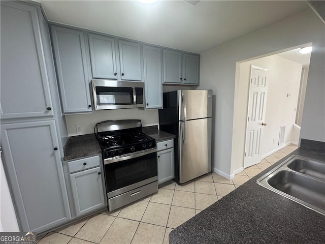 kitchen featuring appliances with stainless steel finishes, dark countertops, a sink, and light tile patterned floors