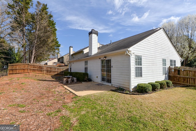 rear view of property with a chimney, a patio, a lawn, and fence