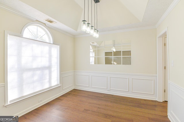 unfurnished dining area featuring a wainscoted wall, crown molding, visible vents, a decorative wall, and wood finished floors