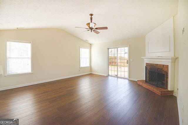 unfurnished living room with lofted ceiling, ceiling fan, baseboards, a brick fireplace, and dark wood finished floors