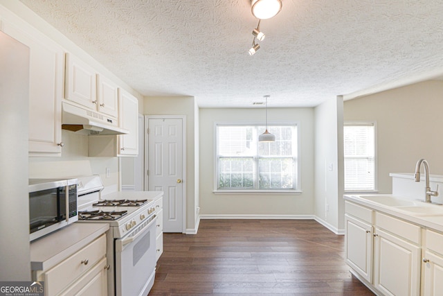 kitchen with white gas stove, under cabinet range hood, dark wood-type flooring, a sink, and stainless steel microwave