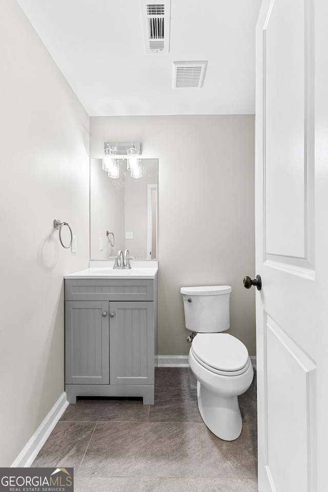 half bath with baseboards, visible vents, vanity, and toilet