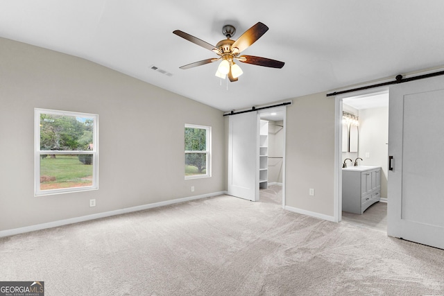 unfurnished bedroom featuring a barn door, visible vents, baseboards, light colored carpet, and a walk in closet