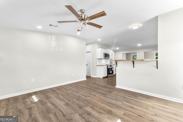 unfurnished living room with visible vents, a ceiling fan, vaulted ceiling, wood finished floors, and baseboards