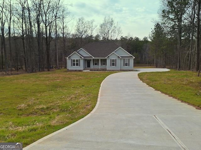 view of front of house with concrete driveway, a forest view, and a front yard