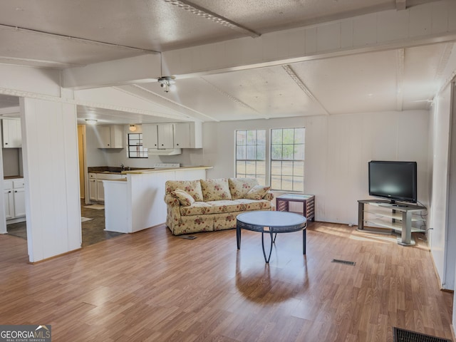 living room with lofted ceiling with beams, light wood finished floors, and visible vents