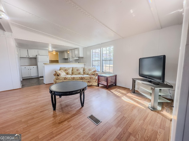 living area with vaulted ceiling, light wood finished floors, and visible vents