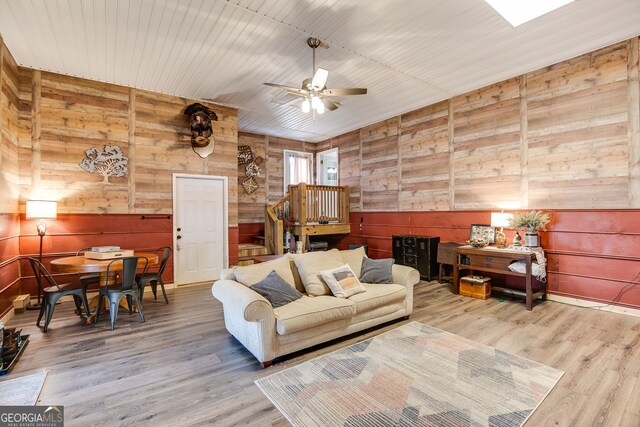 living room with ceiling fan, wood walls, and wood finished floors