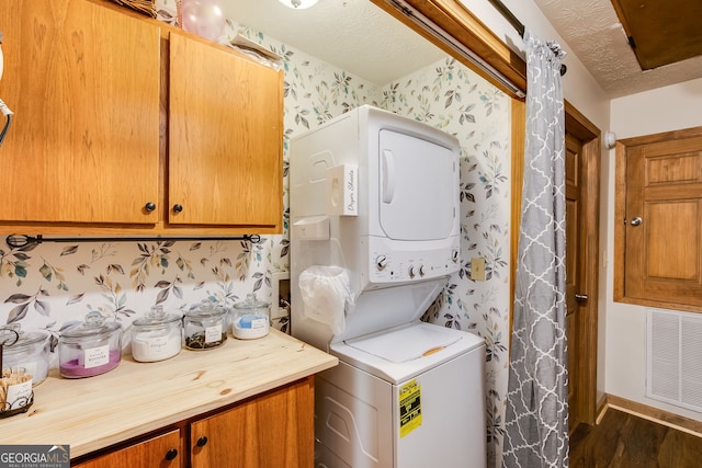 laundry room featuring stacked washer and clothes dryer, visible vents, a textured ceiling, laundry area, and wallpapered walls