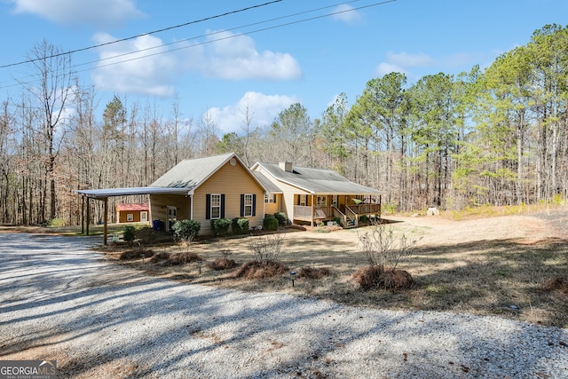 view of side of property featuring driveway, a chimney, a porch, and a view of trees