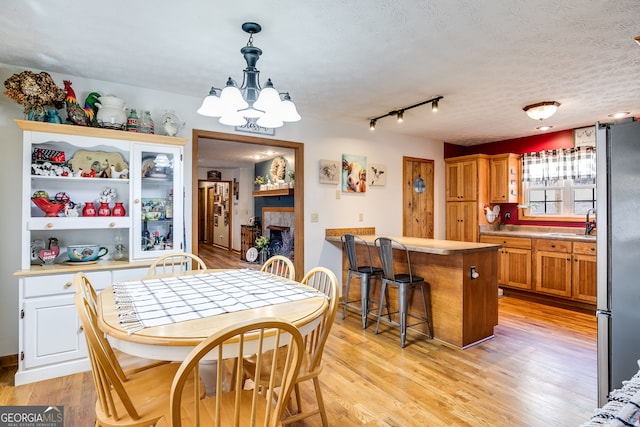 dining room with a textured ceiling, a fireplace, a notable chandelier, and light wood-style floors