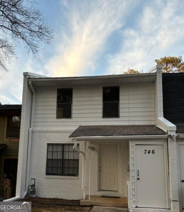 view of front facade featuring roof with shingles, a chimney, and brick siding