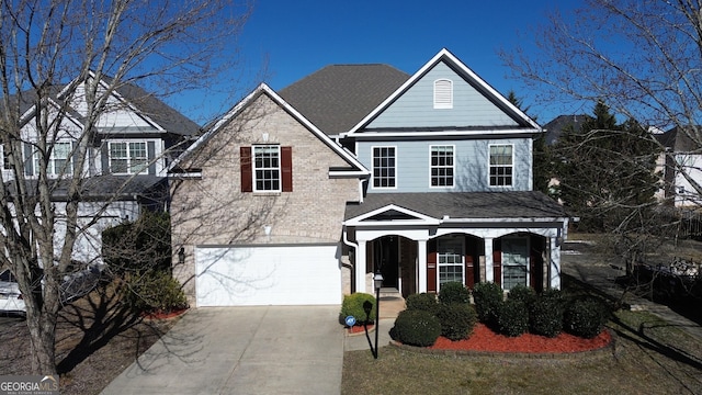 traditional-style house featuring brick siding, a shingled roof, a porch, a garage, and driveway