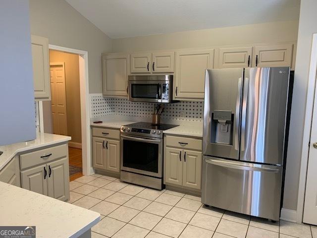 kitchen with light tile patterned floors, backsplash, appliances with stainless steel finishes, and light countertops