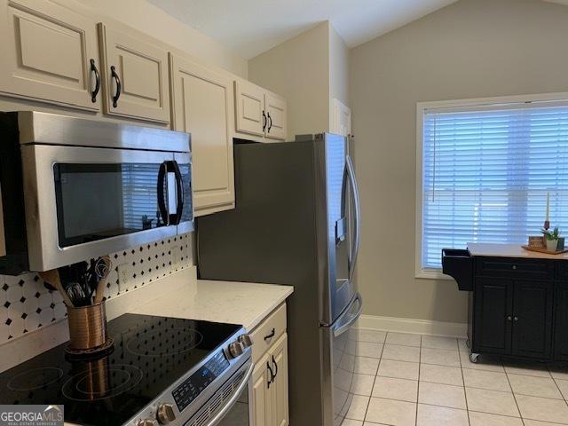 kitchen with baseboards, light countertops, vaulted ceiling, light tile patterned floors, and stainless steel appliances