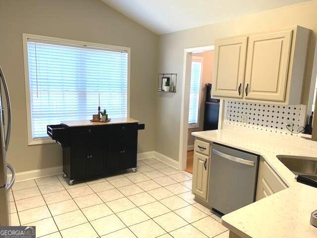 kitchen with light tile patterned floors, baseboards, lofted ceiling, and stainless steel dishwasher