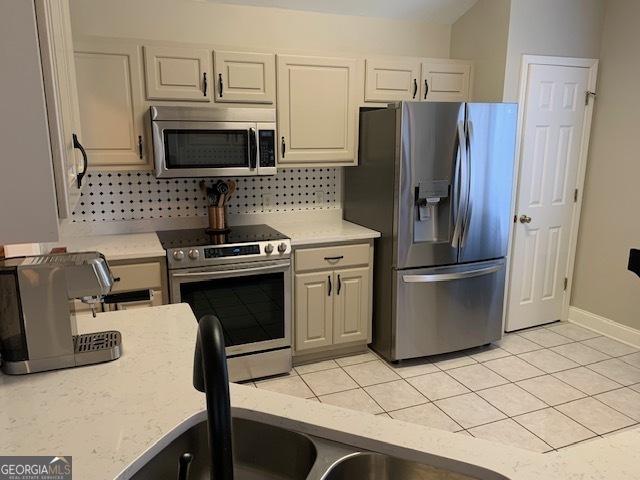 kitchen featuring stainless steel appliances, light tile patterned floors, decorative backsplash, baseboards, and light stone countertops