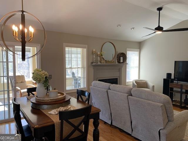 living room featuring lofted ceiling, ceiling fan with notable chandelier, a fireplace, and light wood finished floors