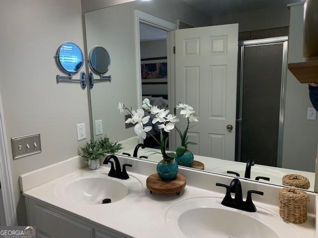 bathroom featuring a shower stall, double vanity, and a sink