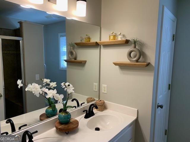 bathroom with a sink, visible vents, double vanity, and a shower stall