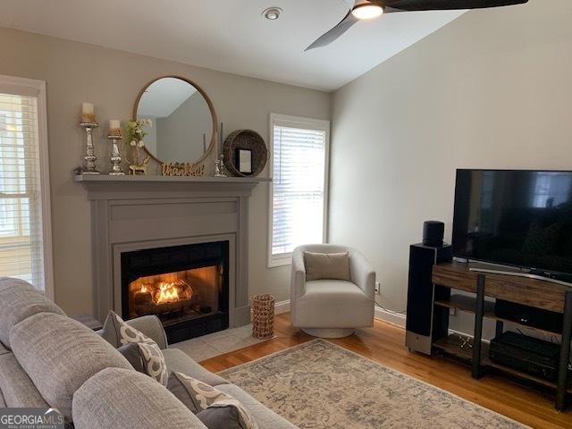 living room with a fireplace with flush hearth, baseboards, ceiling fan, and wood finished floors