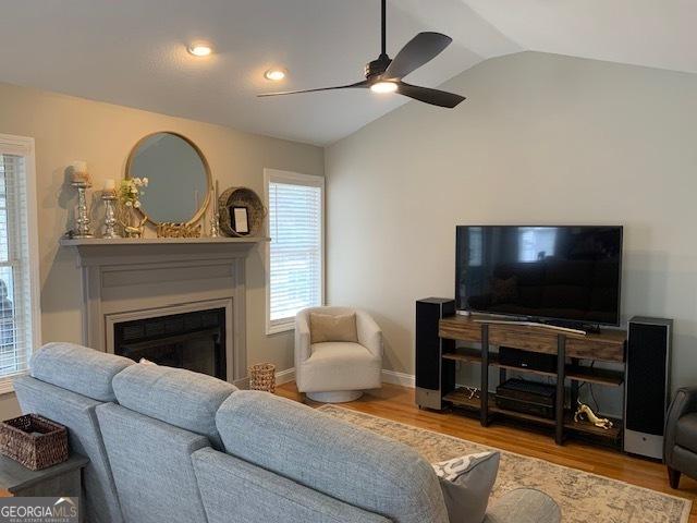 living area with wood finished floors, baseboards, a ceiling fan, lofted ceiling, and a glass covered fireplace