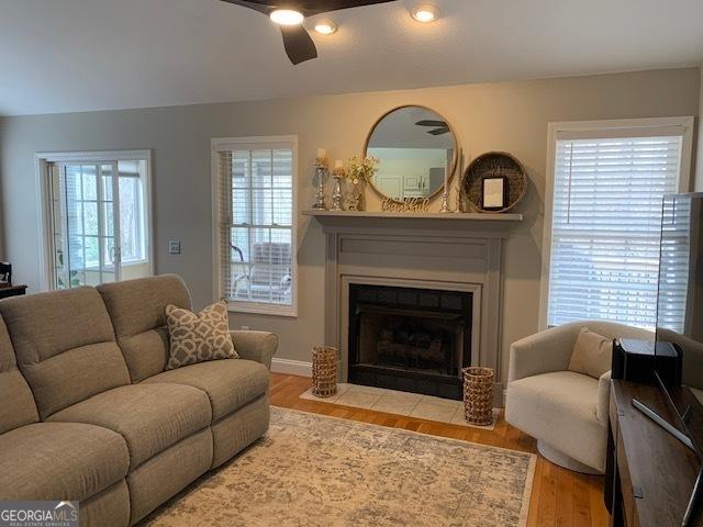 living room featuring a fireplace with flush hearth, baseboards, a ceiling fan, and wood finished floors