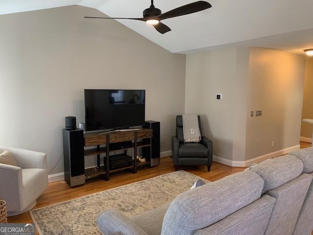 living area featuring baseboards, lofted ceiling, wood finished floors, and a ceiling fan