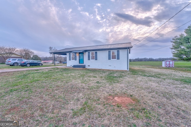 view of front of house with a front yard, a shed, an outdoor structure, brick siding, and metal roof