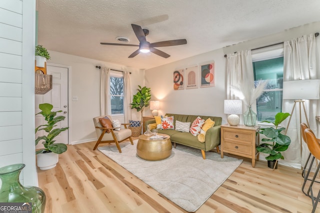 living area with baseboards, a textured ceiling, ceiling fan, and wood finished floors