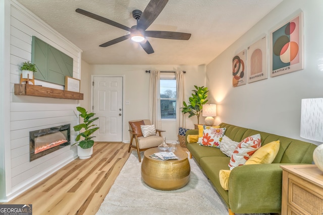 living area featuring light wood-type flooring, a large fireplace, a textured ceiling, and a ceiling fan