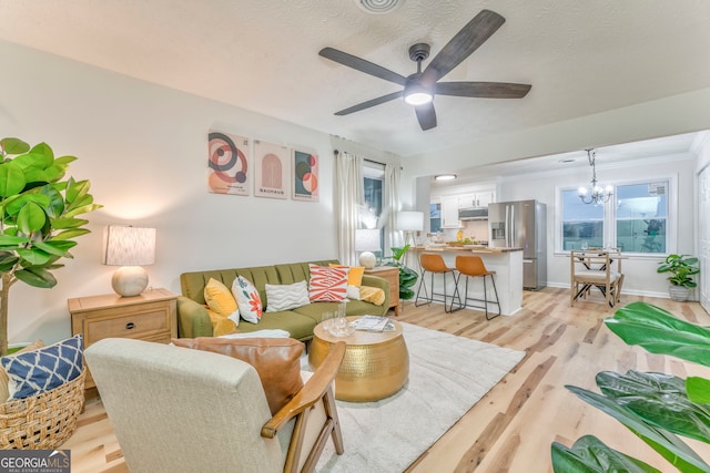 living area with ceiling fan with notable chandelier, light wood-style flooring, a textured ceiling, and baseboards