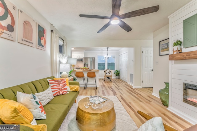 living area with ceiling fan with notable chandelier, visible vents, a fireplace, and light wood-type flooring