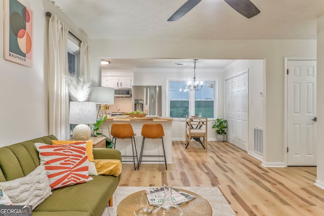 living room featuring visible vents, light wood-style flooring, ceiling fan with notable chandelier, crown molding, and baseboards