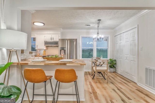 kitchen featuring visible vents, a peninsula, appliances with stainless steel finishes, a kitchen bar, and a chandelier