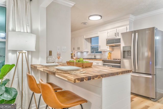 kitchen with a sink, decorative backsplash, butcher block countertops, appliances with stainless steel finishes, and white cabinetry