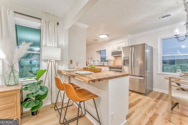 kitchen featuring a breakfast bar, light wood-style flooring, range hood, appliances with stainless steel finishes, and butcher block counters