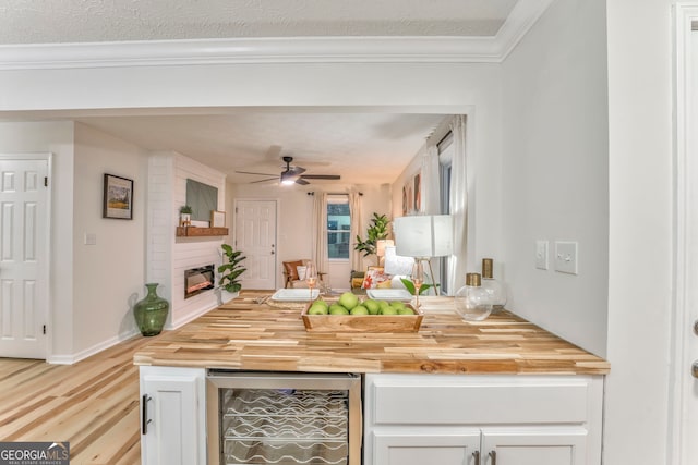 kitchen with beverage cooler, wood counters, a large fireplace, white cabinets, and light wood finished floors